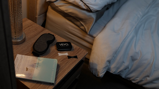 Nasal strips for sleep apnea and snoring placed on a bedside locker with a sleep mask and book.